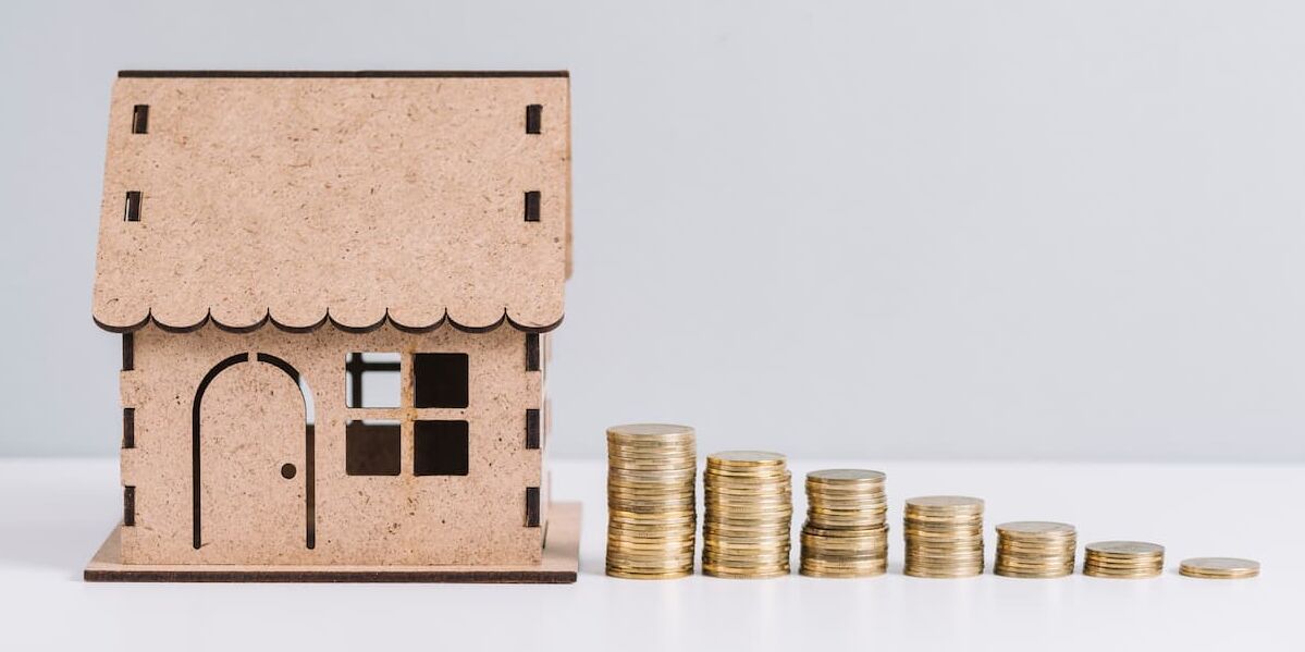 Tokenizzazione immobiliare: modellino di una casa in legno con delle monete a fianco che formano una scala in discesa